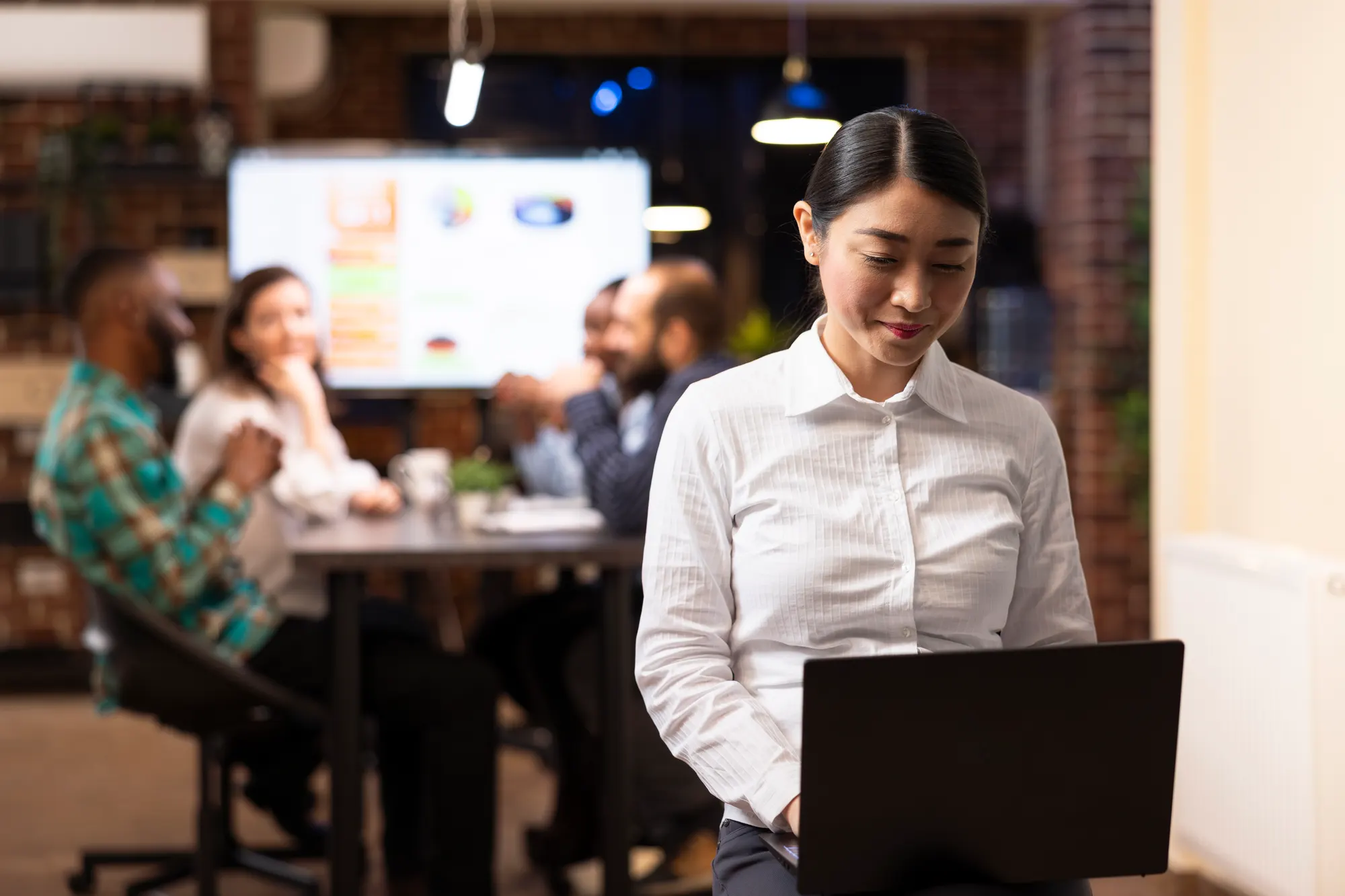 A woman checking performance reports on her laptop while colleagues work behind her